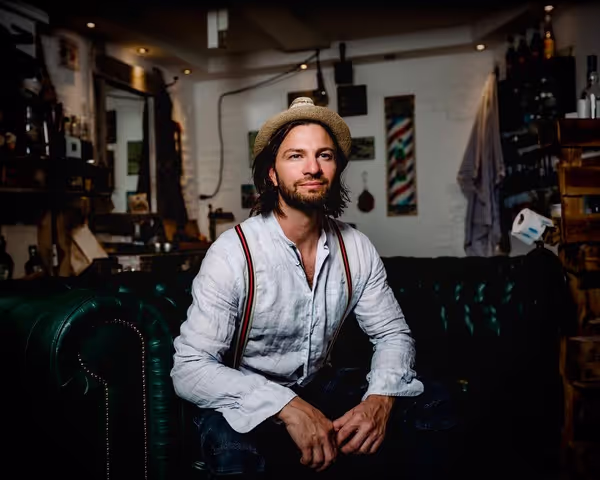 Man with suspenders and fedora sitting on a leather couch