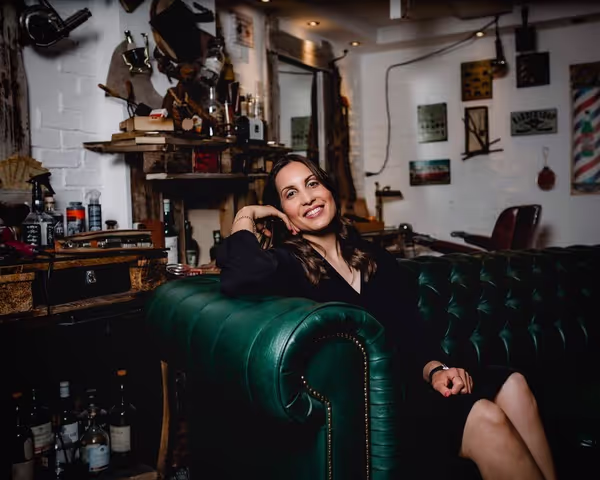 Woman in a black dress with long brown hair sitting releaxed in a green leather couch