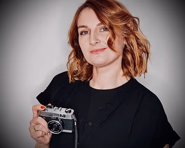 Woman with read hair holding a camera looking directly into the camera