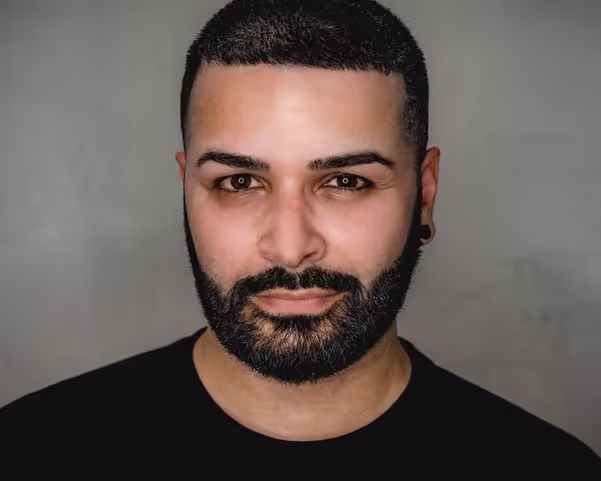 Man with short black hair and a gage in his left ear looking directly into the camera