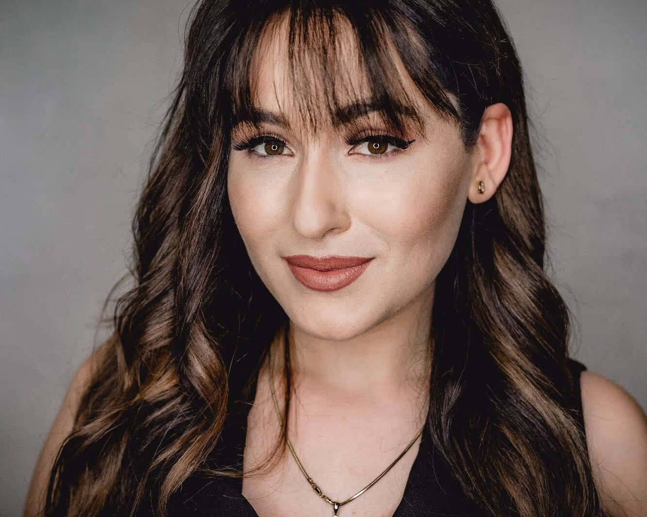 Woman with brown hair and slight banks smirking into the camera