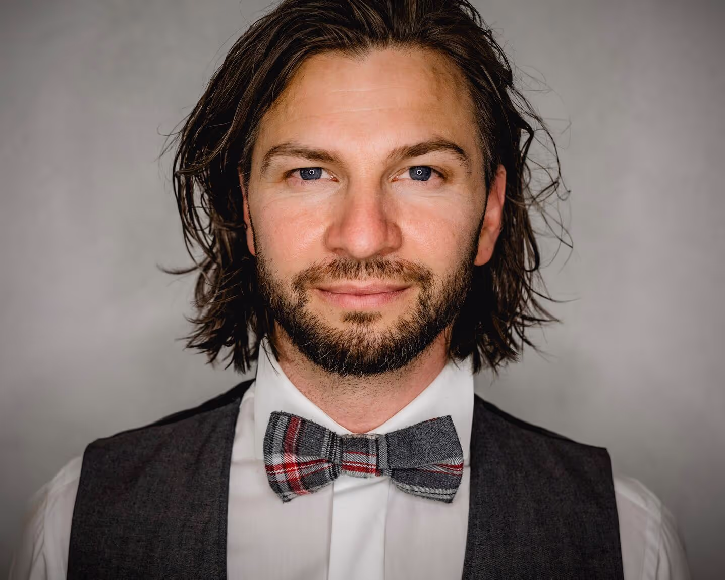 A male person with bowtigh, whiteshirt and vest. Long Hair looking directly into the Camera