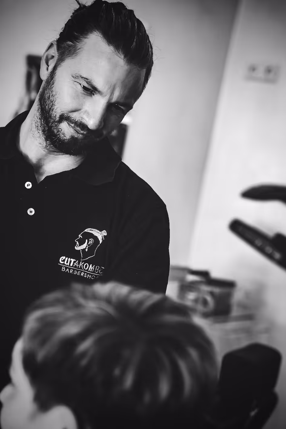 Man with a black T-shirt looking looking at the side of a head to probably asses the haircut