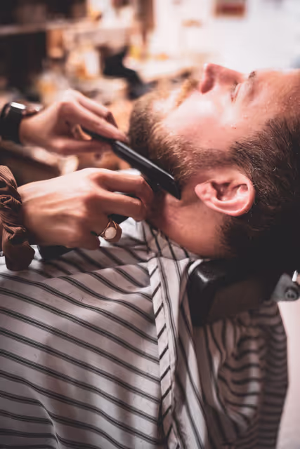 A man in a barbershop who"s beard is getting brushed.