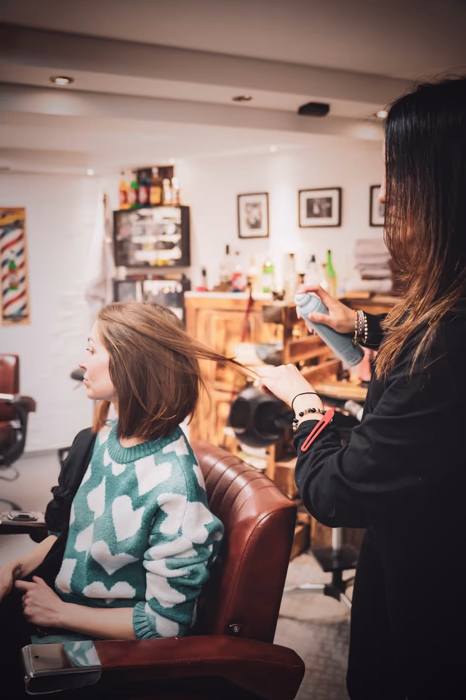 A woman sitting in a barber chair getting her hair dried with a hairdryer 